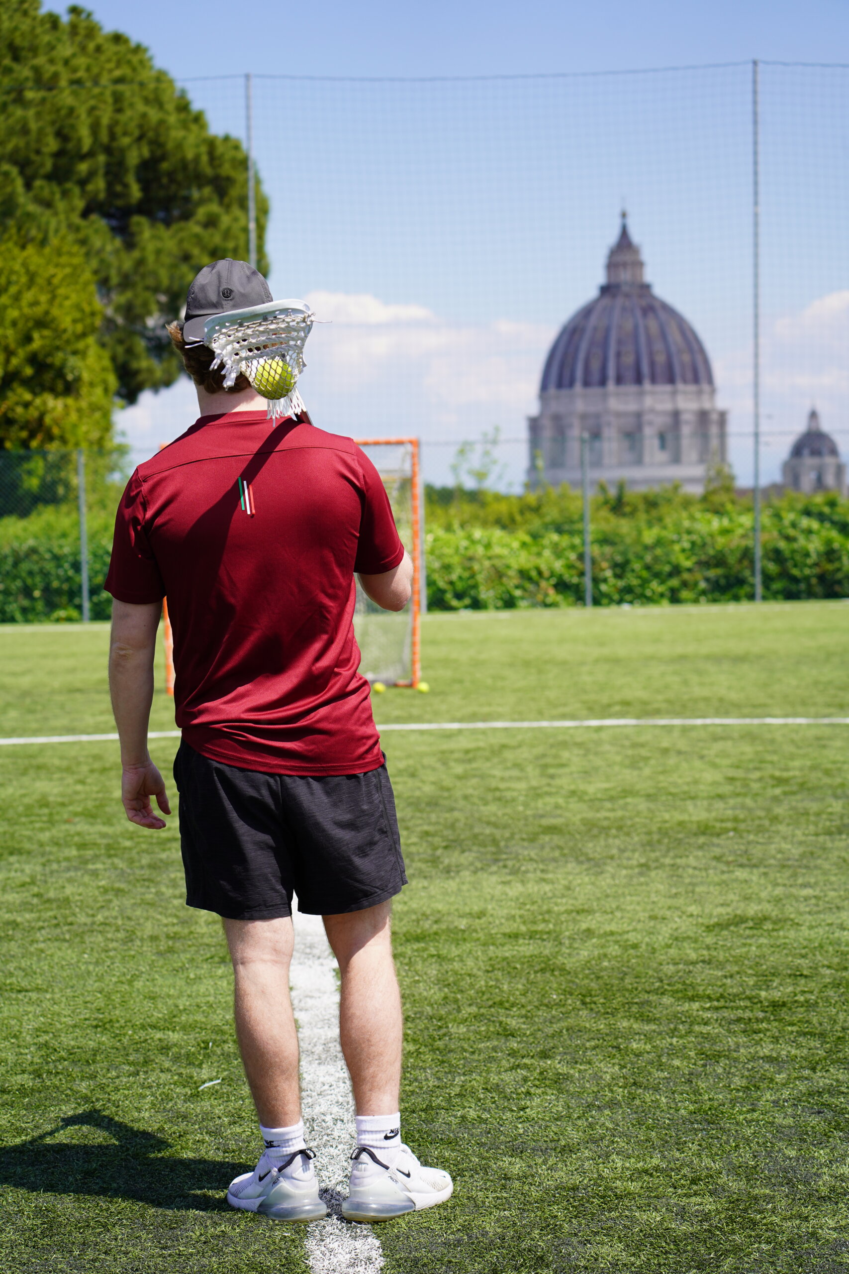 Rome City Institute lacrosse player on the pitch with St. Peter's Basilica dome in the distance